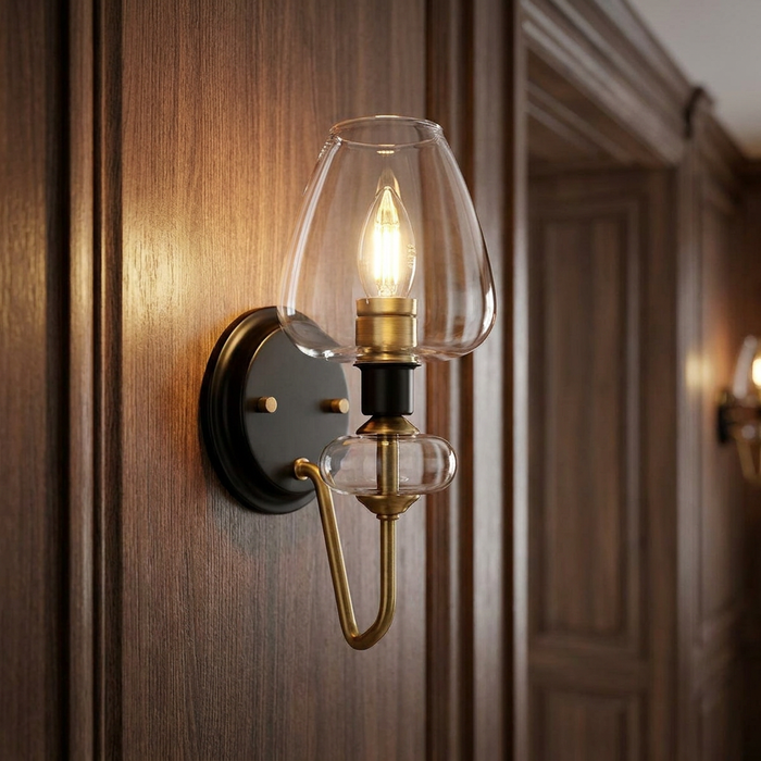 Aged brass wall light with a clear glass hurricane shade glowing against dark wood paneling.