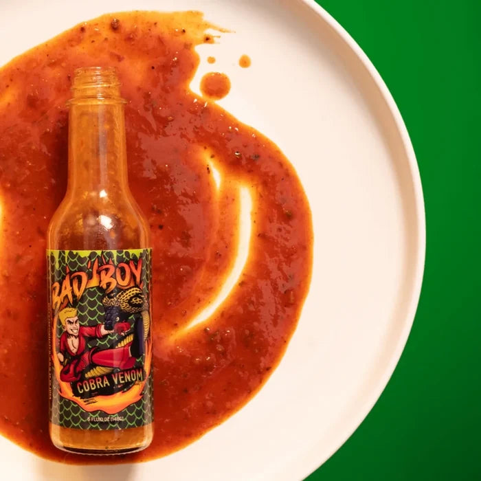 Bad Boy Cobra Venom hot sauce bottle with spicy orange-red sauce splatter on white plate