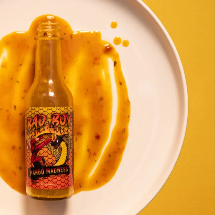 Bad Boy Mango Madness hot sauce bottle with fresh yellow peppers on white plate