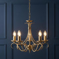 Endon Bernice 5-light antique brass chandelier with lit candle bulbs against a dark blue paneled wall.