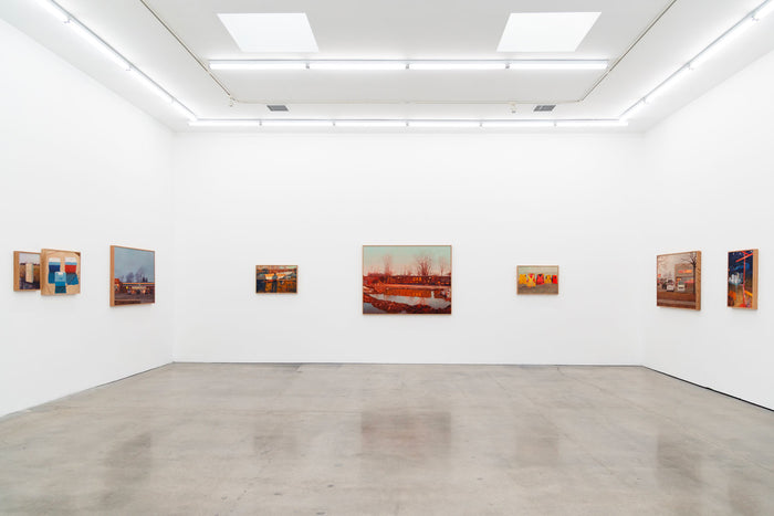 A modern art gallery with white walls and a polished concrete floor showcases pieces like the Charity Postcard by Pat Perry. The evenly spaced, framed artworks are illuminated by ceiling lights and three rectangular skylights, embodying the spirit of contemporary artistry.