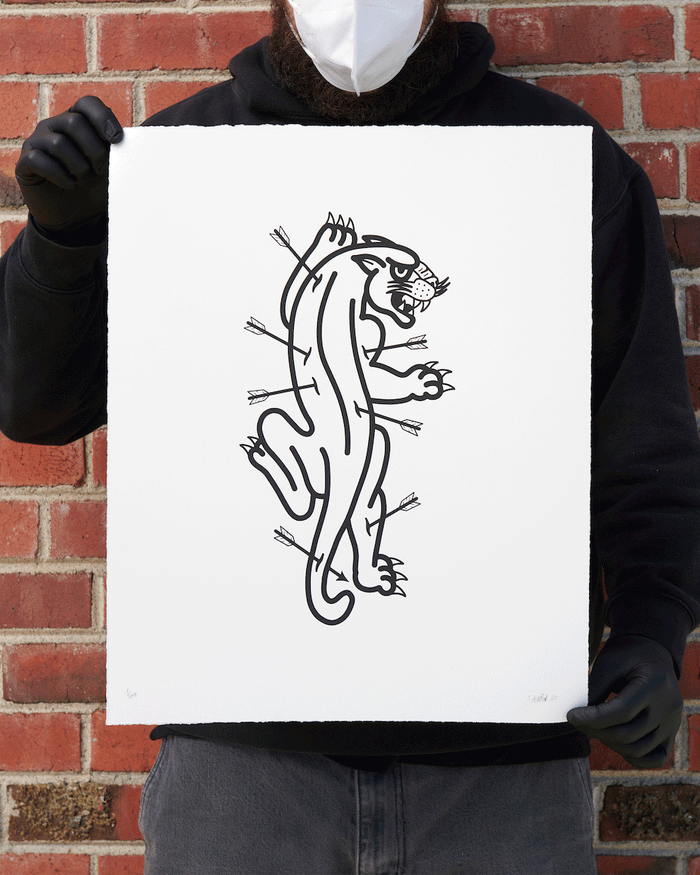 A person in a black hoodie, gloves, and face mask holds Panther & Arrows from Christopher Martins exclusive Two Print Set. The design features a panther in black line style pierced with arrows against a brick wall backdrop.