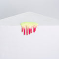 Dan Lams Mini #10 features a neon green and pink spiky design with a dripping hot glue-like texture, gently hanging over the edge of a white surface against a light gray background, giving it a soft and tactile, melting appearance.