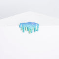 The Mini #14 by Dan Lam is a small abstract sculpture in blue and green, crafted from acrylic and resin with sponge-like spikes. It sits on a white geometric surface, giving a dripping effect against the plain backdrop.