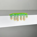 Dan Lams Mini #260 features a whimsical, spiky, green and blue caterpillar with purple and yellow accents crawling over the edge of a white surface. This 2023 mixed media piece showcases bold colors contrasting vividly against the neutral background.
