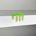 Dan Lams vibrant Mini #278, a 2023-inspired mixed media creation, features a spiky, artificial caterpillar with a gradient from green to purple, hanging over a white edge against a plain gray background.