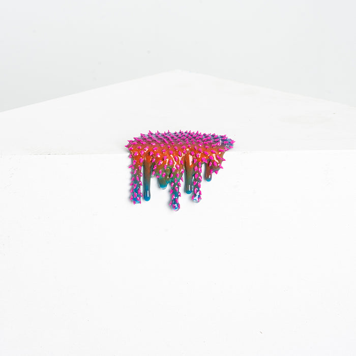 Dan Lams Mini #28 features a colorful, spiky, abstract resin design with vivid pink, blue, and red hues. The piece appears to drip off a white surface against a light background.