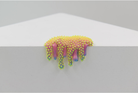 Dan Lams Mini #3-57 is a resin-like sculpture with vibrant pink and yellow spots, accented by hints of blue, creating a drippy effect reminiscent of melting paint. It elegantly adorns a white corner surface, achieving a minimal and clean aesthetic.