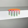 Dan Lam - "Mini #317" by Dan Lam is a colorful, spiked artwork resembling melting pink and purple slime with yellow dots, draped over the edge of a white shelf against a gray background—an imaginative mixed media piece created in 2023.