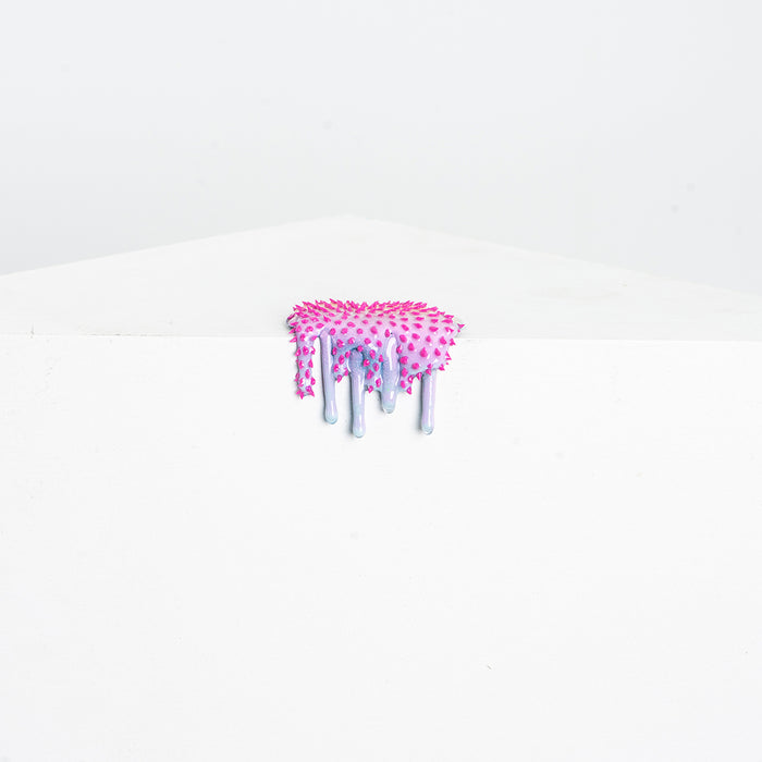 Dan Lams Mini #38 is a pink and silver drip-shaped resin creation with a textured, beaded surface on a white geometric base set against a light gray background, giving the appearance of melting or dripping over the edge.