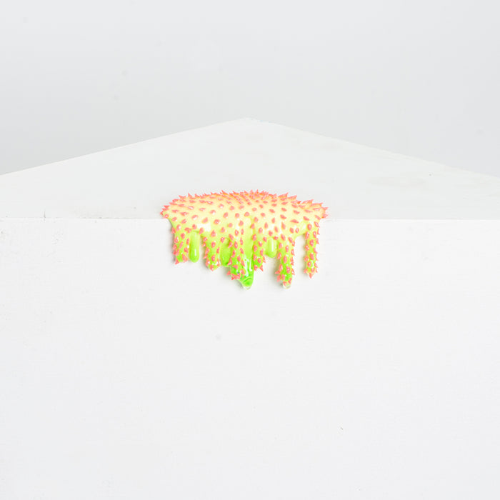 Dan Lams Mini #39 features a bright, textured object that resembles dripping paint in fluorescent pink and green, oozing like hot glue over the edge of a stark white geometric surface against a light gray background.