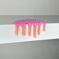 Dan Lams Mini #407 is a pink and orange mixed media piece (2 x 3 3/4 x 2 inches) with a textured, studded pattern and glossy finish, evoking melted paint drips over a white shelf for a striking visual effect against its minimalist background.
