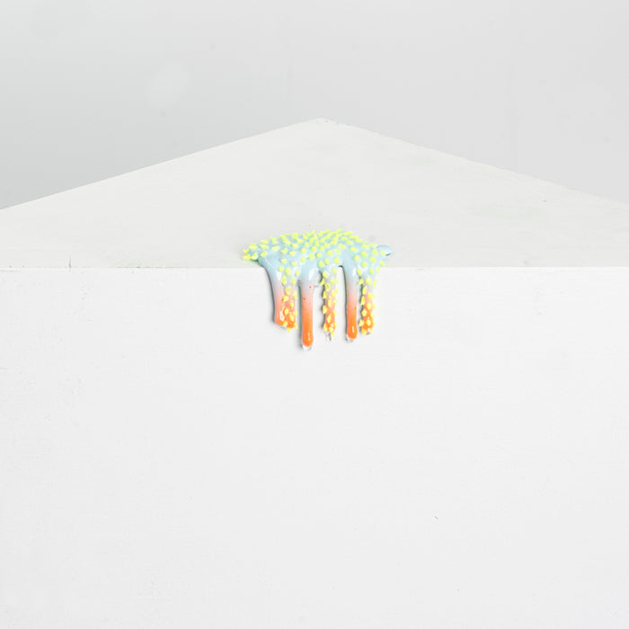 Dan Lams Mini #43, resembling a colorful, spiky sea creature, features green and orange resin draping over a white surface against a light gray background.