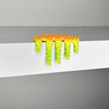 Dan Lams Mini #468, crafted in 2023 using mixed media, is a small textured piece. It features a bright yellow to orange gradient with spiky elements resembling melting goo dripping over the edge of a white shelf against a gray background.