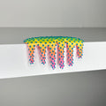 Dan Lam’s "Mini #506" is a captivating mixed media piece from 2023, featuring a vibrant, spiky, slime-like form that drips over the edge of a white surface. Showcasing innovative artistry, the object displays a stunning gradient from yellow to pink, accented by blue spikes tipped with small white spheres.