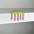 Mini #520" by Dan Lam is a colorful mixed media sculpture featuring vibrant yellow and green hues, with pink and blue-tipped spikes resembling dripping slime. Hanging over the edge of a white surface against a gray background, this striking 2 x 3 x 1 3/4 inch artwork was created in 2023.