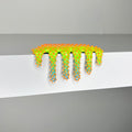 Dan Lam's "Mini #609" is a 2023 mixed media piece featuring neon green and orange goo-like forms with blue accents and spiked protrusions, dripping over the edge of a white shelf. This striking artwork from Dan Lam blends bold color and texture for an eye-catching effect.