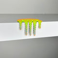 Dan Lam's "Mini #619," a vibrant neon green and orange spiked slime sculpture crafted in 2023, drips over the edge of a white shelf set against a gray background.