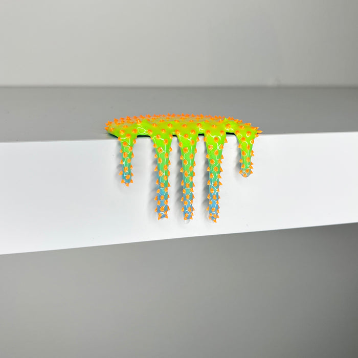 Dan Lam's "Mini #619," a vibrant neon green and orange spiked slime sculpture crafted in 2023, drips over the edge of a white shelf set against a gray background.