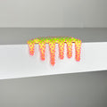 The vibrant Mini #652 by Dan Lam, a multicolored mixed media piece, features star shapes transitioning from yellow to pink. This imaginative 2023 design innovation elegantly drips over the edge of a white shelf.