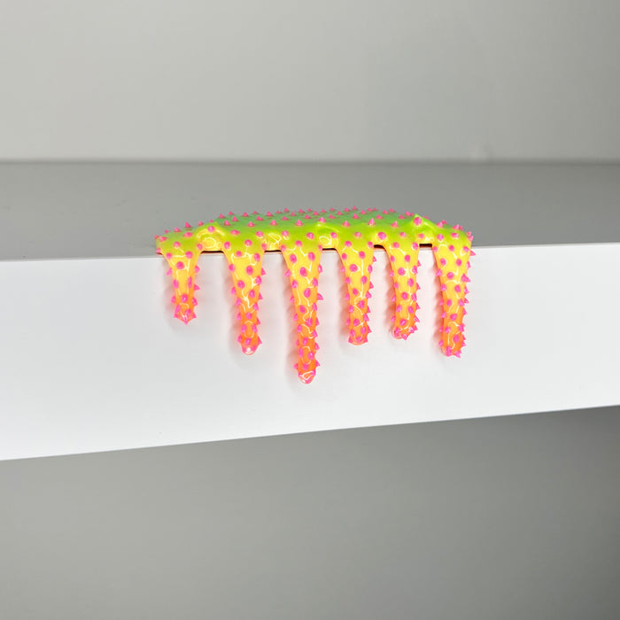 The vibrant Mini #652 by Dan Lam, a multicolored mixed media piece, features star shapes transitioning from yellow to pink. This imaginative 2023 design innovation elegantly drips over the edge of a white shelf.