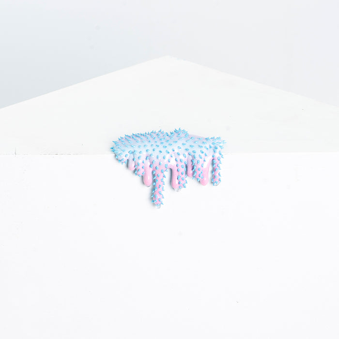 Mini #6 by Dan Lam, a surreal resin blob with blue spikes and pink drips, sits whimsically on a white surface amidst a minimalist white background.