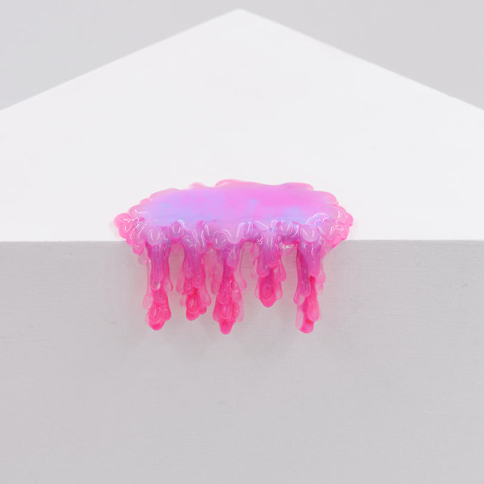 A glossy, pink and purple resin-like substance appears to melt and drip like acrylic glue over the edge of a white geometric surface against a plain background in Dan Lam’s "Mini #7.04" sculpture.