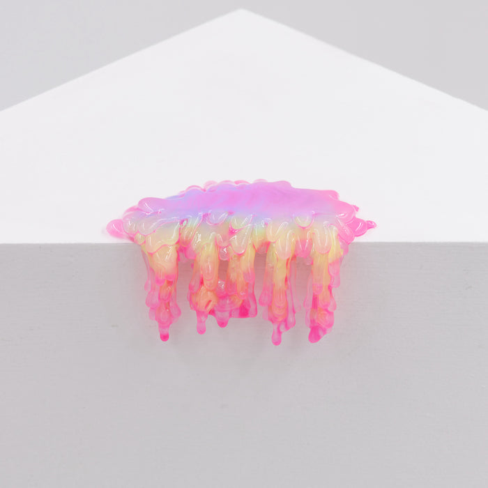 Iridescent, glossy pink, yellow, and purple resin slime from Dan Lam’s "Mini #7.08" drips over the edge of a white geometric surface against a plain light background.