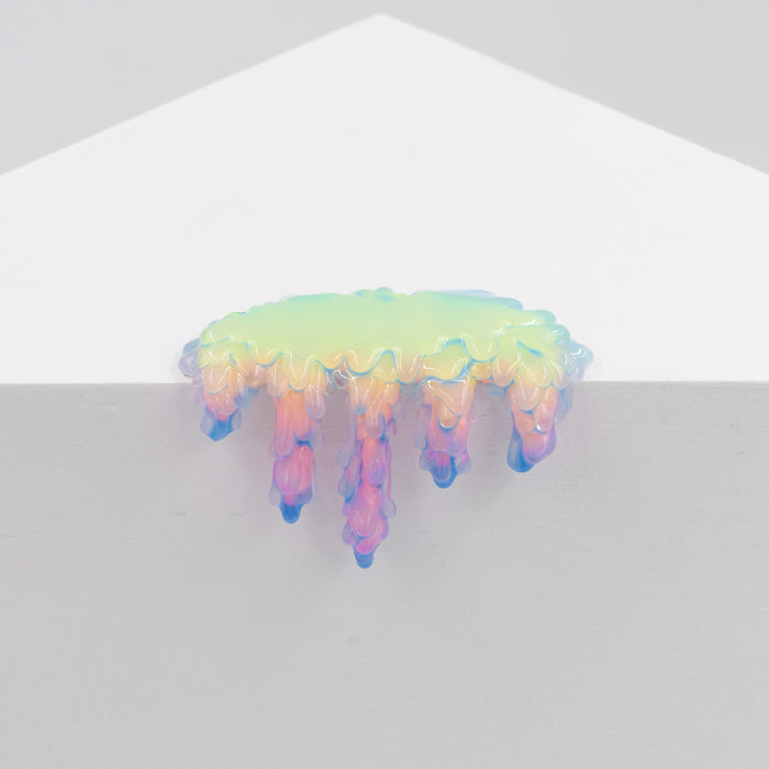 Dan Lams Mini #7.30 features a small, iridescent, cloud-like form on a white surface with colorful dripping tendrils in shades of pink, purple, and blue. The understated elegance is enhanced by the plain light gray background.