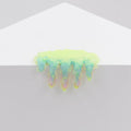 The Dan Lam Mini #7.44 sculpture, an iridescent, drippy resin piece with green, blue, and pink hues, rests elegantly on a white surface like a melting puddle formed by delicate acrylic layers.