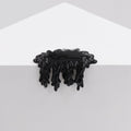 A glossy black liquid drips over a white geometric structure, resembling resin, with an organic flow. This striking effect in the artwork Mini #7.67 by Dan Lam combines acrylic art and natural forms against a plain backdrop.