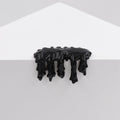 Dan Lam's "Mini #7.71" features glossy black resin dripping over the edge of a white geometric surface, forming irregular downward shapes against a plain gray background.