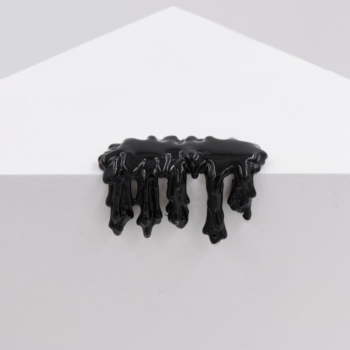 Dan Lam's "Mini #7.71" features glossy black resin dripping over the edge of a white geometric surface, forming irregular downward shapes against a plain gray background.