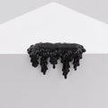A glossy, black, resin-like sculpture—Dan Lam's "Mini #7.74"—appears to drip over the edge of a white geometric surface against a light gray background.