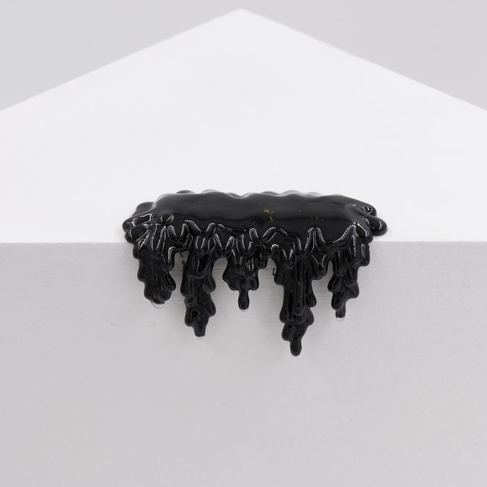 A glossy, black, resin-like sculpture—Dan Lam's "Mini #7.74"—appears to drip over the edge of a white geometric surface against a light gray background.