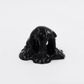 Dan Lams Mini #7.91 features a mound of glossy black liquid resembling acrylic paint, set against a plain white background. The thick liquid flows smoothly, creating a shiny surface.