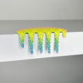 A neon green and blue spiked, goo-like object drips over the edge of a white surface, its form covered in pink-tipped spikes and set against a plain gray background. "Mini #855" by Dan Lam (2023) is a striking mixed media creation that captures otherworldly texture and vibrant energy.