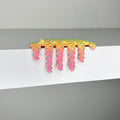 Dan Lam's 'Mini #906'—a yellow and pink spiky sculpture—drips playfully over the edge of a white shelf against a plain gray background, exemplifying the artist's distinctive mixed media style in this 2023 piece.