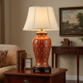 Terracotta ceramic table lamp with a white lattice pattern and cream shade on a wooden side table in a living room.