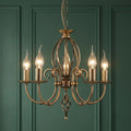 Aged brass 5-light chandelier with flame-shaped bulbs against a dark green paneled wall.