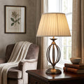 Aged brass cage table lamp with a pleated cream shade illuminating a cozy living room corner.