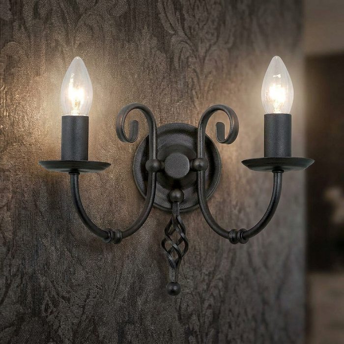 Traditional black wrought iron twin arm wall light with candle bulbs on textured wallpaper.