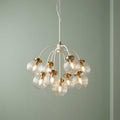 Elstead Cosmos nine-light brass and cream ceiling pendant with ribbed glass globes on a light green background.