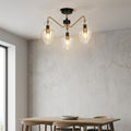 Armand 3-light brass and black semi-flush ceiling light with clear glass shades over a dining table.