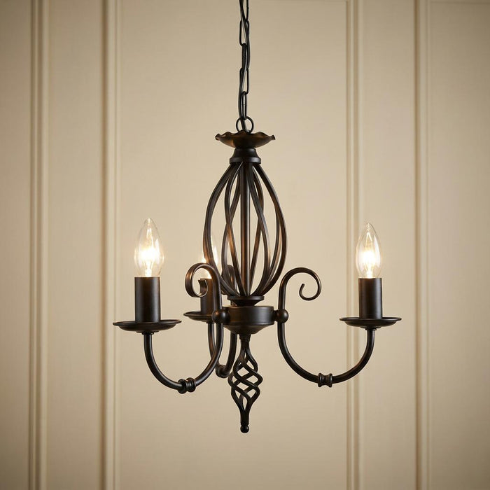 Black three-light chandelier with scrolled metal arms and a caged central detail, lit against a cream wall.