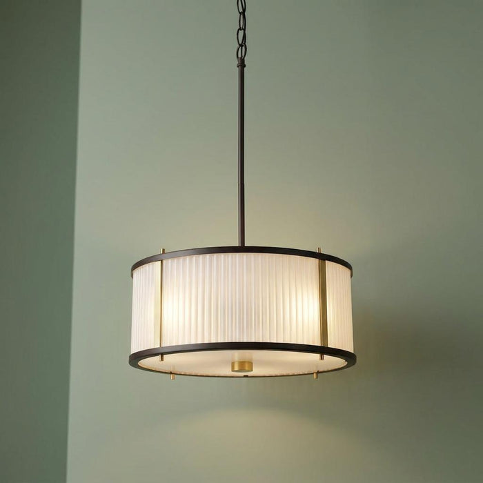 A bronze drum-style ceiling pendant with a ribbed glass shade, hanging against a soft green wall.