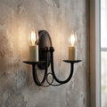 Elstead Minster 2-light black wall sconce with glowing candle-style bulbs on a rustic, textured wall.