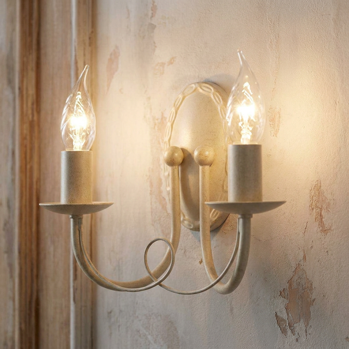 Traditional ivory and gold 2-light wall sconce with candle bulbs mounted on a distressed, textured wall.