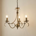 Endon Bernice antique brass 3-light chandelier with decorative curved arms and glowing candle bulbs against a plain wall.