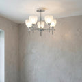 Chrome semi-flush ceiling light with five frosted glass shades illuminated against a textured grey wall.